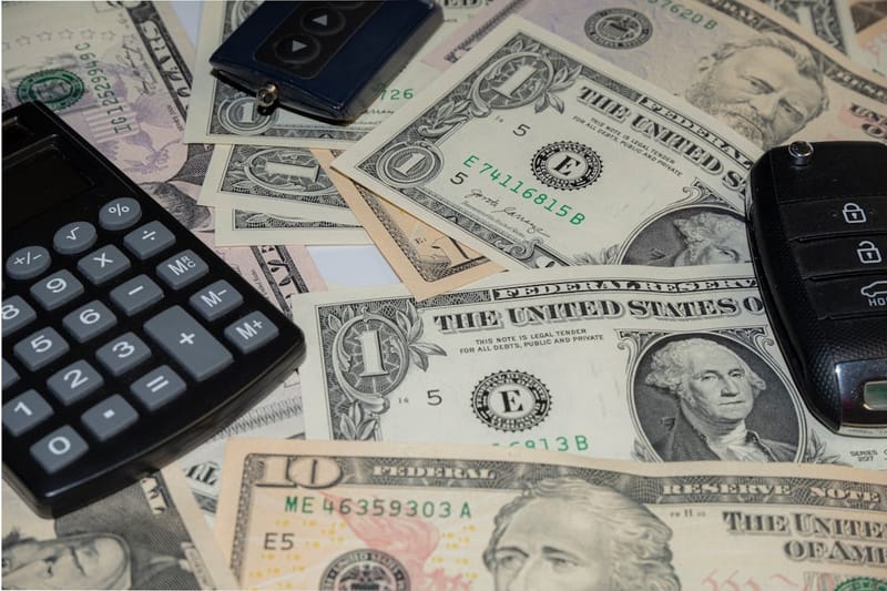 Calculadora y llaves de carro sobre billetes - costos de alquiler